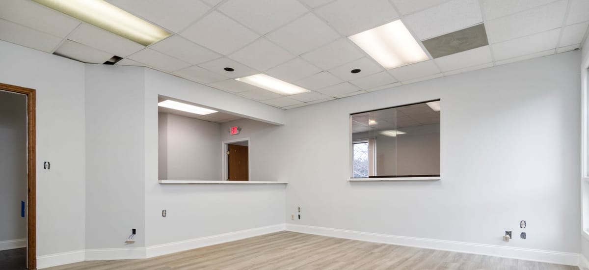 An empty commercial office interior, freshly painted, with a grid ceiling and reception hatch