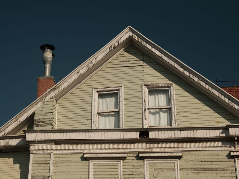 The gable end of an older clapboard house, paint weathered and flaking off the boards