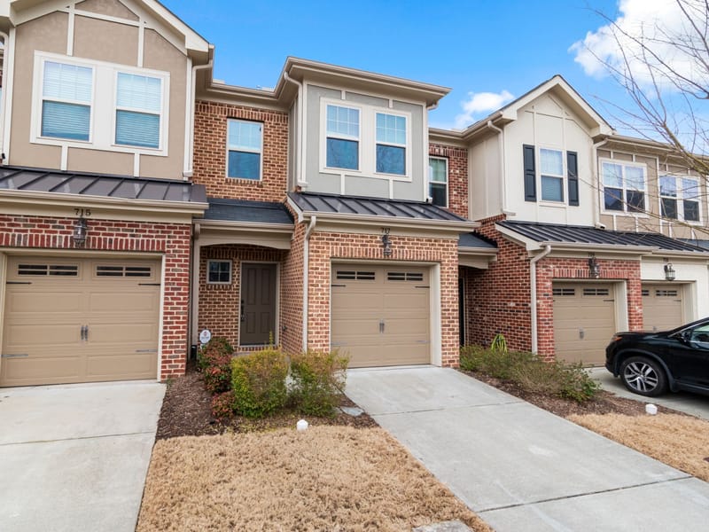 A row of brick townhouses with attached single garages and short driveways