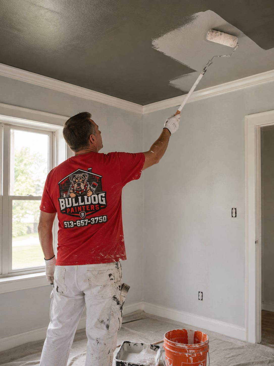 A Bulldog Painters painter rolling a ceiling with an extension pole, the fresh coat cutting across the old