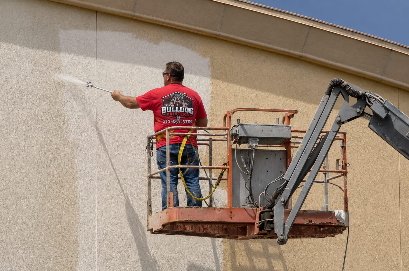 A Bulldog Painters painter spraying a commercial building exterior from a boom lift