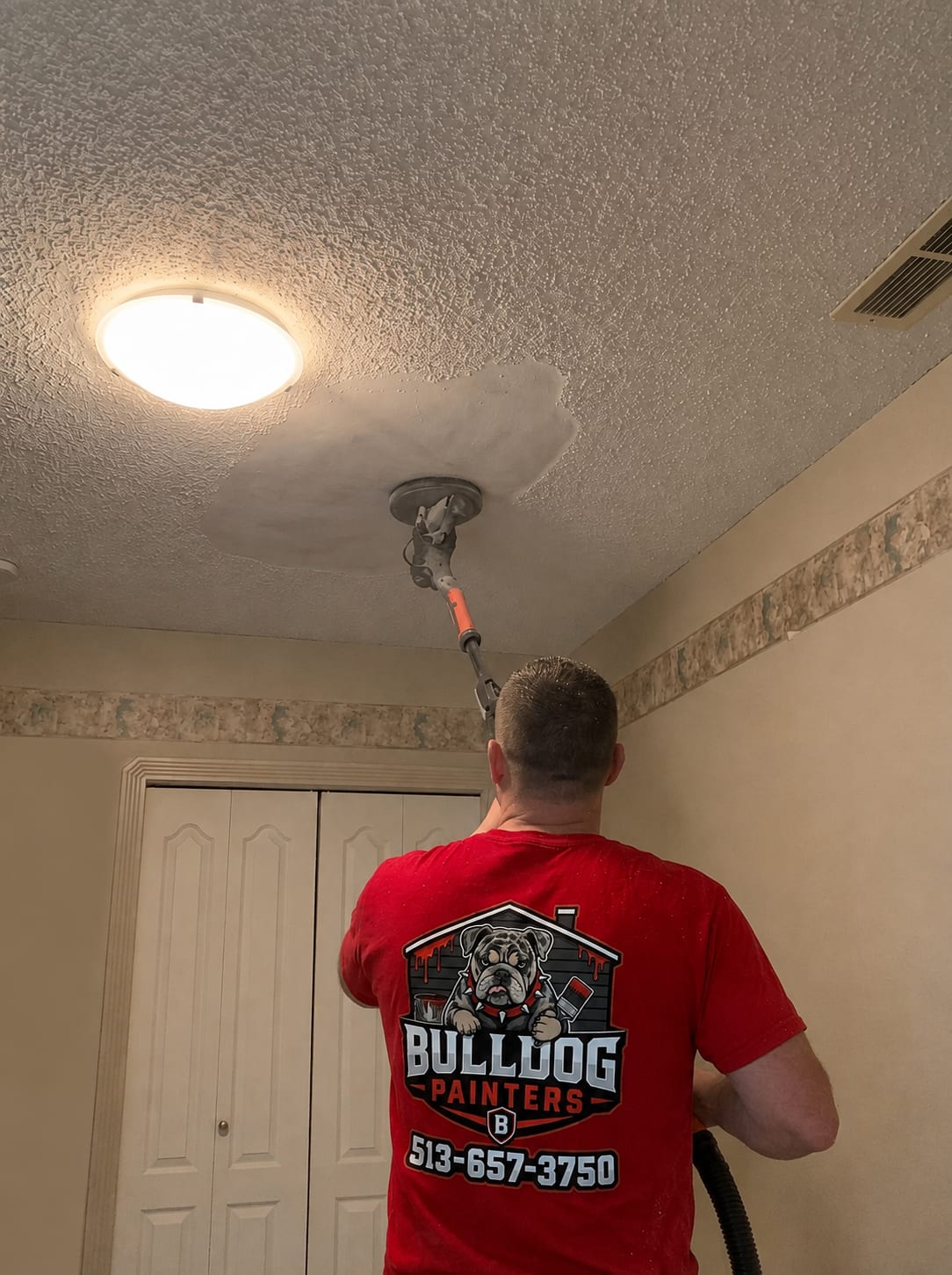 A Bulldog Painters painter working overhead on a textured ceiling