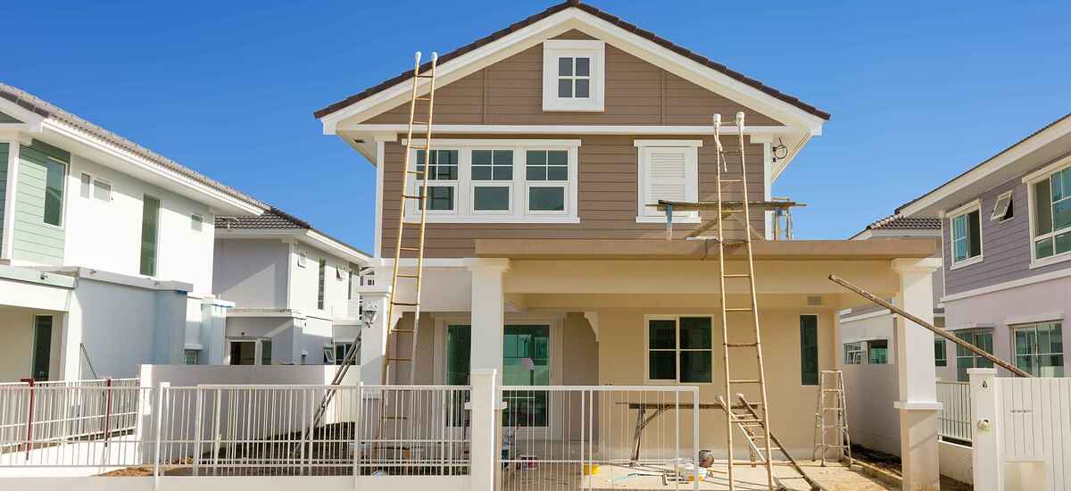 A two-storey house part way through an exterior repaint, ladders up against the gable and staging along the porch roof