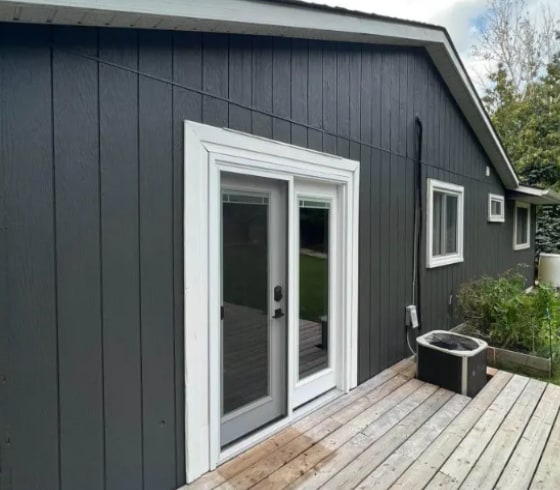 The same house exterior after painting — charcoal siding with white trim around the patio door