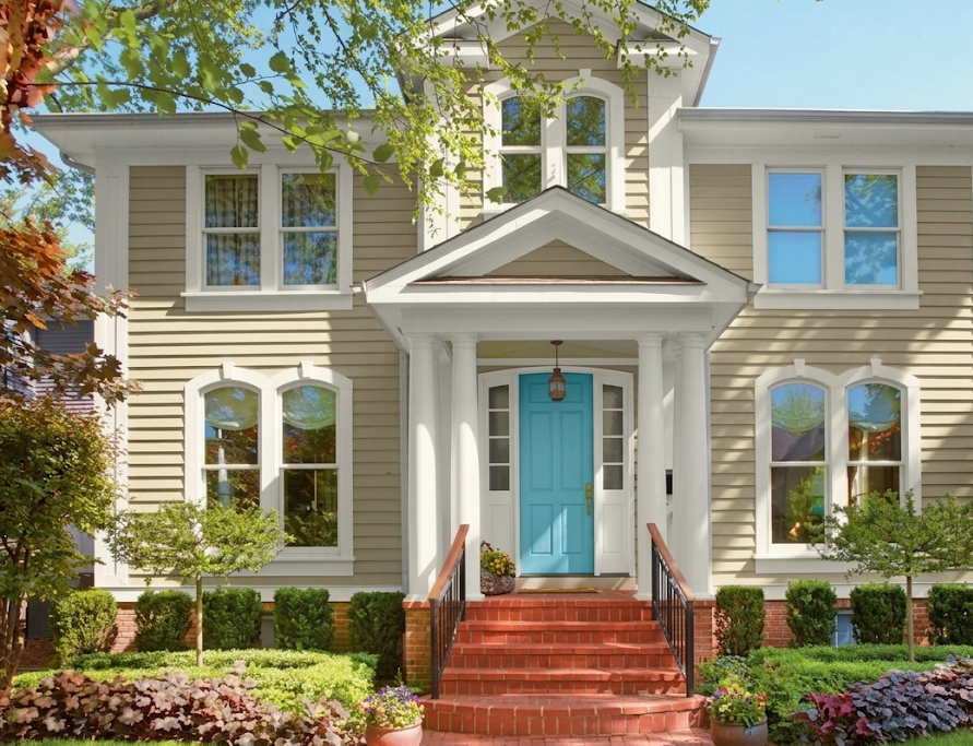 A house exterior before painting — olive-stained board siding with bare wood trim around the patio door